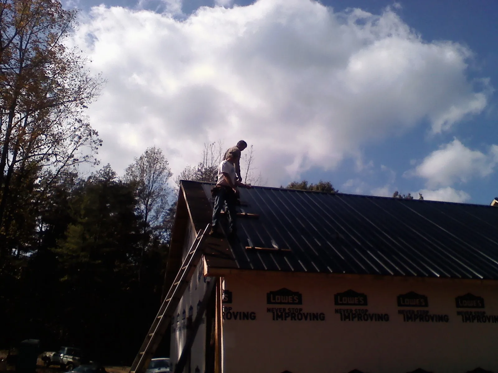 Roofer fastening dark metal panels high against a cloudy sky in Pembroke